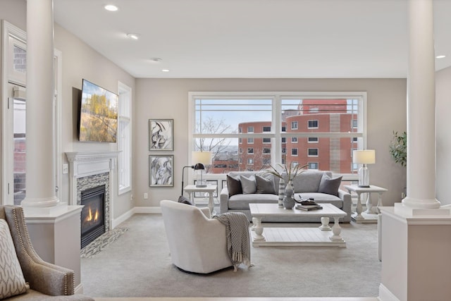 living room with a glass covered fireplace, a wealth of natural light, ornate columns, and light carpet