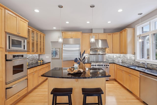 kitchen featuring light brown cabinets, under cabinet range hood, built in appliances, a warming drawer, and a sink