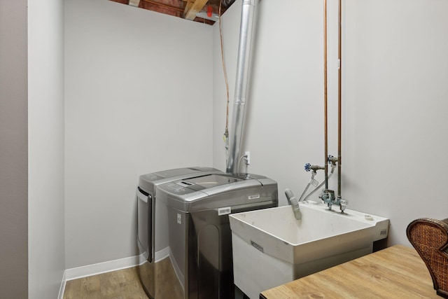 clothes washing area with independent washer and dryer, a sink, wood finished floors, baseboards, and laundry area