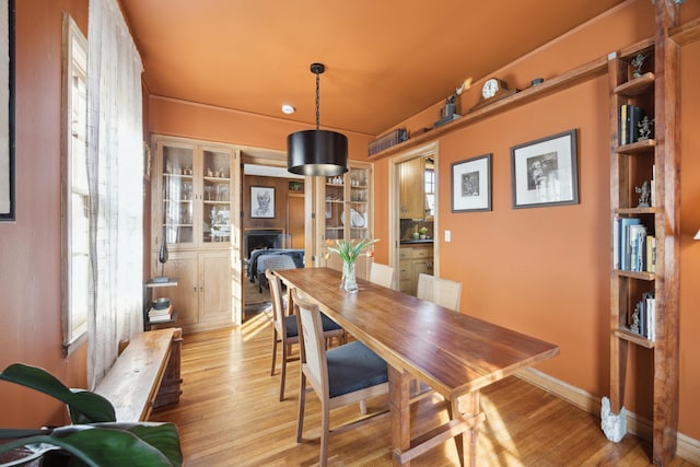 dining room featuring baseboards, a fireplace, and light wood finished floors