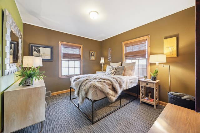 bedroom with multiple windows, visible vents, baseboards, and dark colored carpet