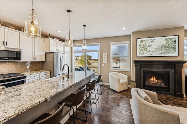 kitchen featuring a breakfast bar area, dark wood-style floors, light stone countertops, appliances with stainless steel finishes, and backsplash