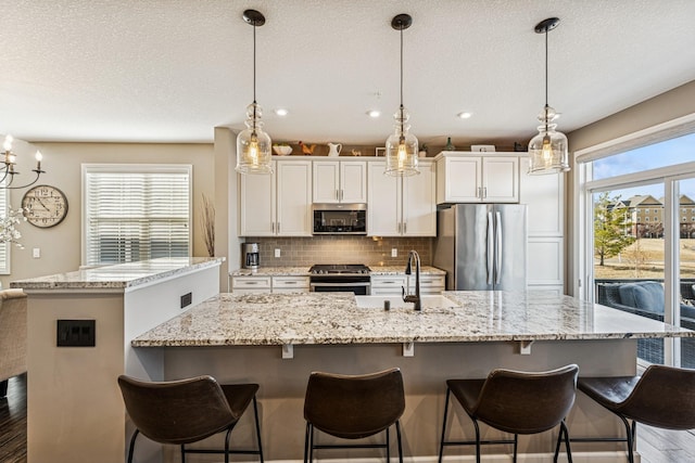 kitchen with a sink, decorative backsplash, a center island with sink, and stainless steel appliances