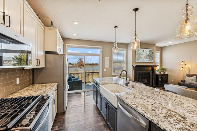 kitchen with dark wood-type flooring, a sink, light stone counters, open floor plan, and appliances with stainless steel finishes