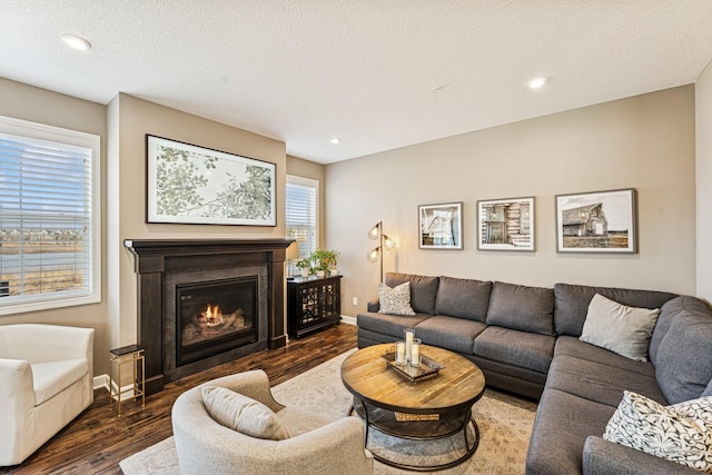 living area with a textured ceiling, a glass covered fireplace, wood finished floors, recessed lighting, and baseboards