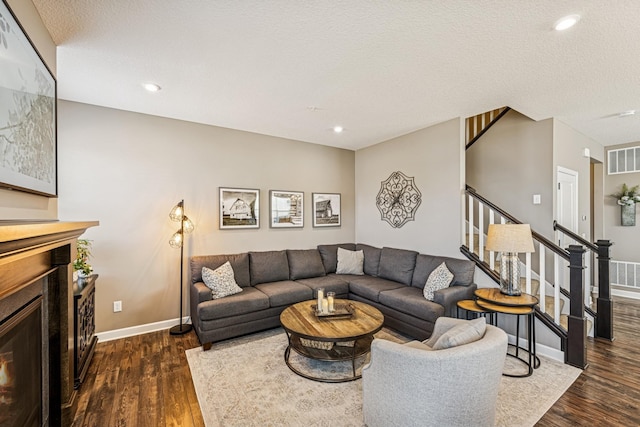 living area featuring stairway, visible vents, dark wood-style flooring, and a lit fireplace