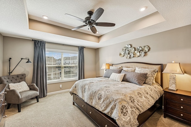 bedroom with a tray ceiling, light carpet, and a textured ceiling