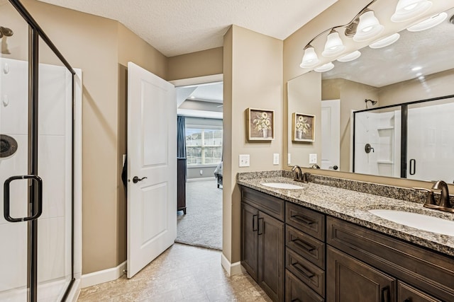 bathroom featuring a textured ceiling, double vanity, a stall shower, and a sink