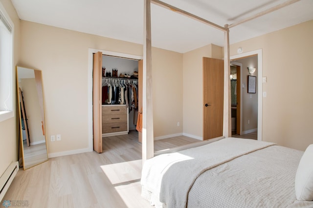 bedroom with baseboards, light wood finished floors, a closet, a baseboard heating unit, and a walk in closet