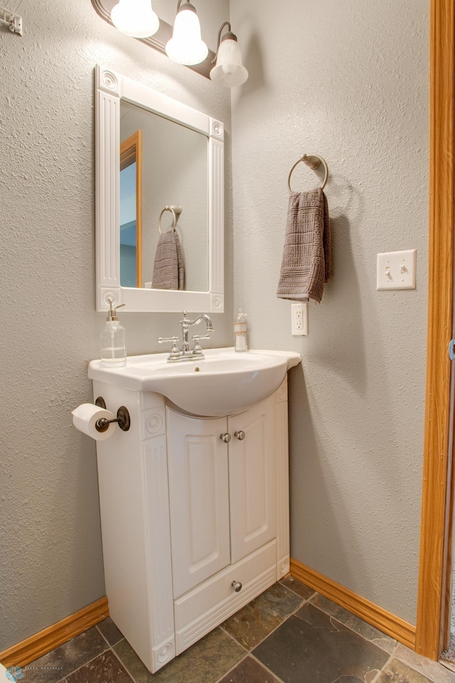 bathroom featuring baseboards, stone tile floors, and vanity