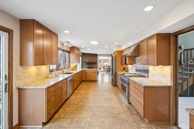 kitchen featuring a sink, stainless steel appliances, wall chimney exhaust hood, decorative backsplash, and light stone countertops