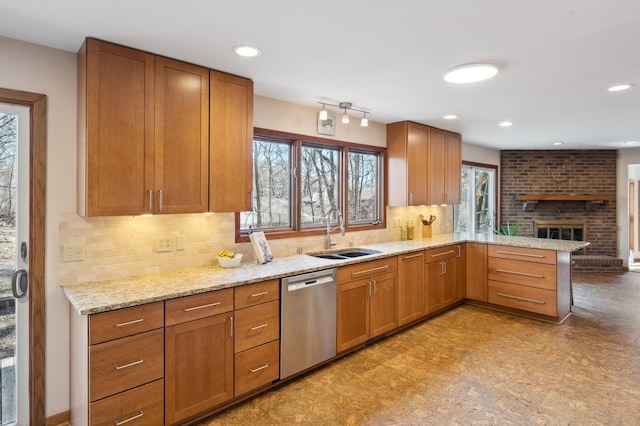 kitchen with light stone countertops, a peninsula, a sink, stainless steel dishwasher, and a brick fireplace