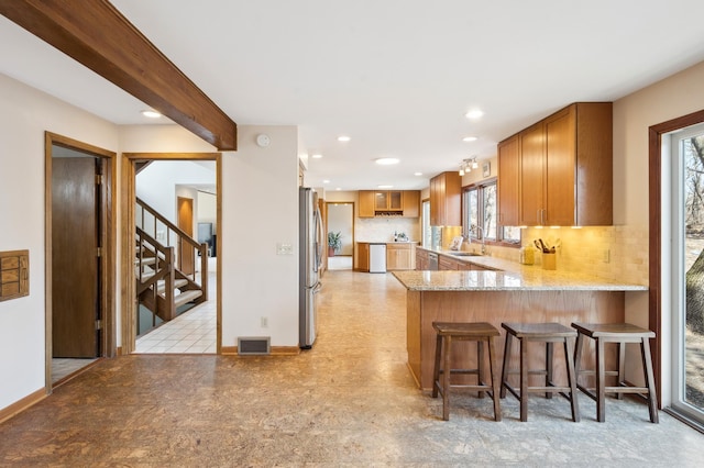 kitchen featuring visible vents, light stone counters, brown cabinets, freestanding refrigerator, and a sink