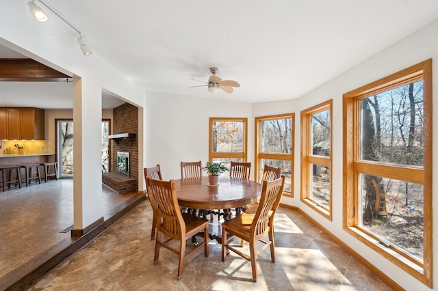 dining area with plenty of natural light, a brick fireplace, baseboards, and ceiling fan