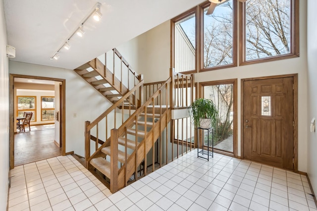 entryway with stairs, track lighting, light tile patterned floors, and baseboards