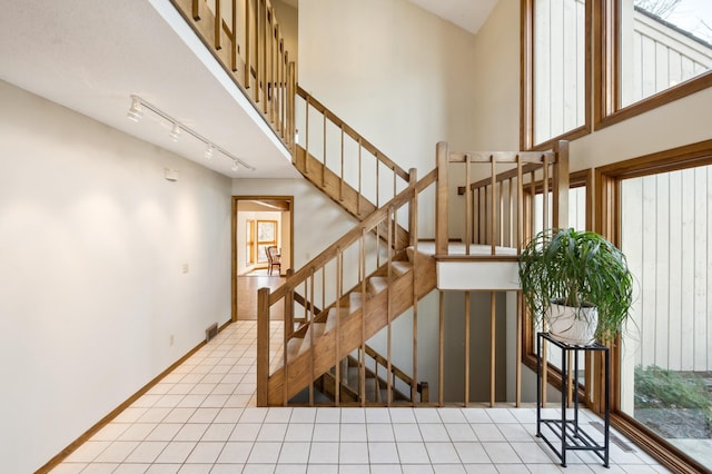 stairway with track lighting, a high ceiling, baseboards, and tile patterned floors