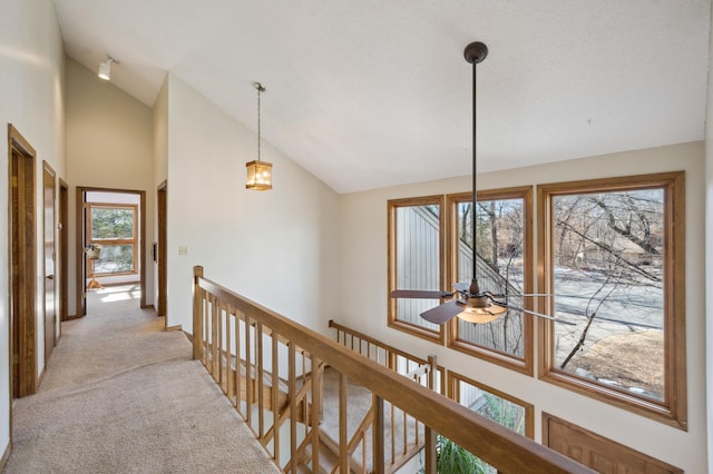 hallway featuring high vaulted ceiling, an upstairs landing, and light carpet