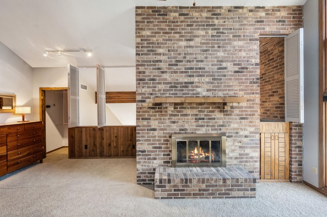 carpeted living room with track lighting, a brick fireplace, visible vents, and wood walls