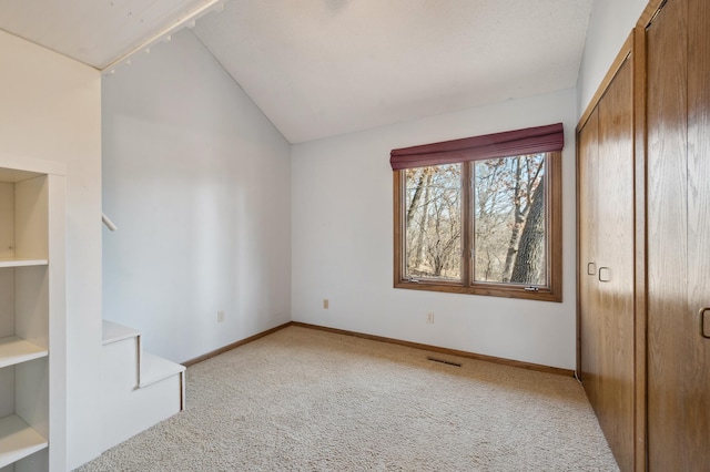 unfurnished bedroom with lofted ceiling, light colored carpet, baseboards, and a closet