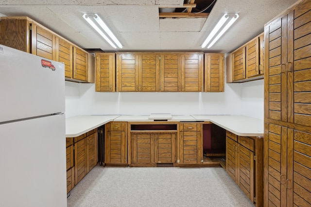 kitchen featuring light countertops, brown cabinetry, and freestanding refrigerator