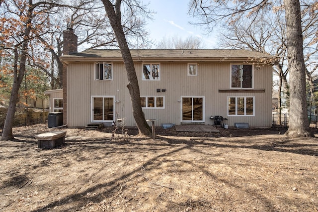 back of property with central AC, a chimney, and a shingled roof