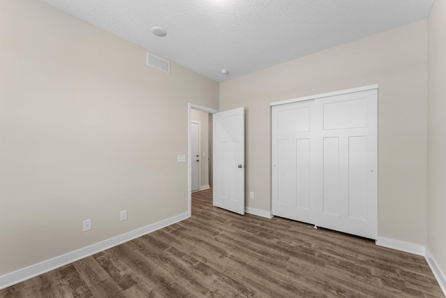 unfurnished bedroom with visible vents, baseboards, a closet, and wood finished floors