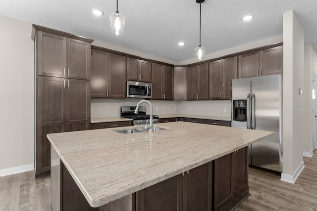 kitchen with a sink, stainless steel appliances, dark brown cabinetry, and light wood finished floors