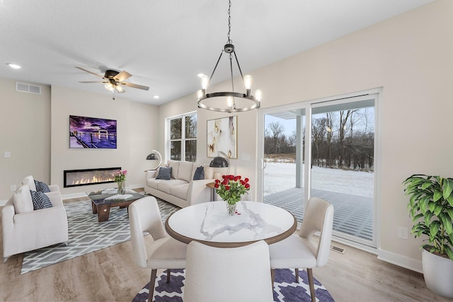 dining space featuring a glass covered fireplace, wood finished floors, visible vents, and a wealth of natural light