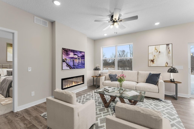 living room with visible vents, baseboards, wood finished floors, a glass covered fireplace, and a textured ceiling