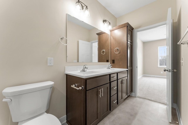 bathroom with double vanity, toilet, baseboards, and a sink