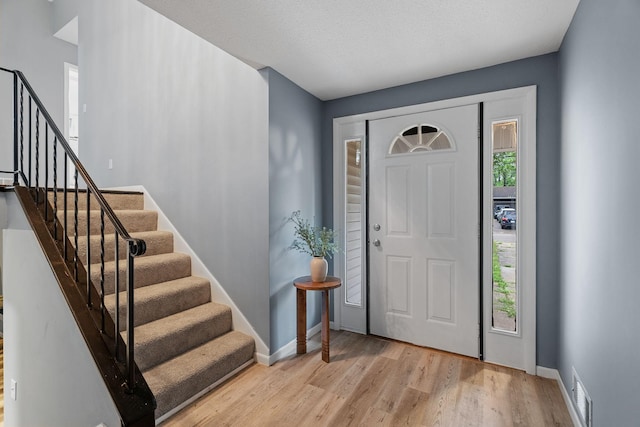 entrance foyer with stairway, plenty of natural light, visible vents, and wood finished floors