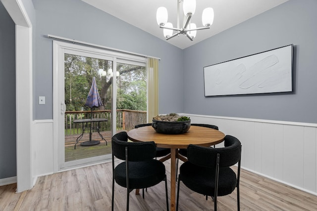 dining room featuring a wainscoted wall, light wood-style flooring, lofted ceiling, and an inviting chandelier