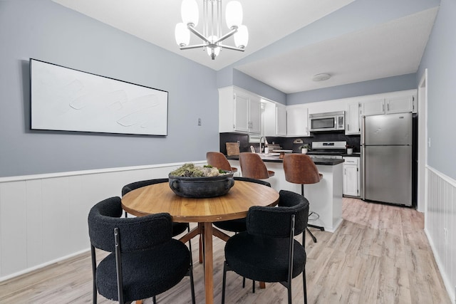 dining space with an inviting chandelier, light wood-style flooring, and a wainscoted wall