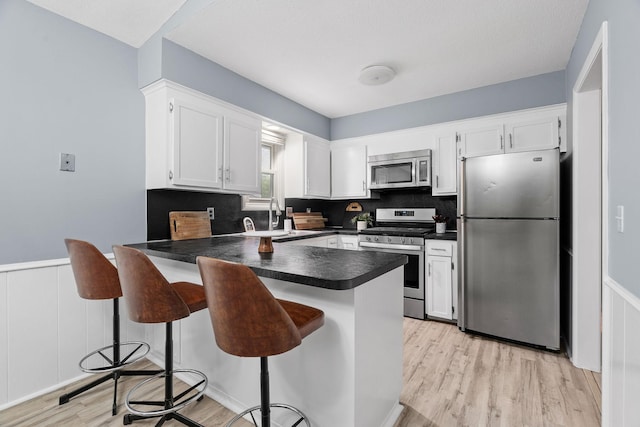 kitchen with light wood-style flooring, a sink, dark countertops, stainless steel appliances, and a peninsula