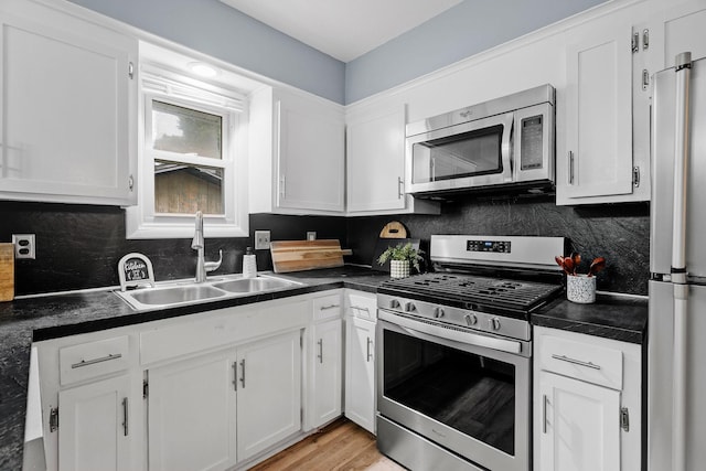 kitchen with dark countertops, backsplash, appliances with stainless steel finishes, white cabinets, and a sink