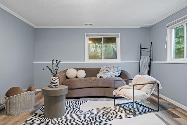 living room with wood finished floors, visible vents, baseboards, a textured ceiling, and crown molding