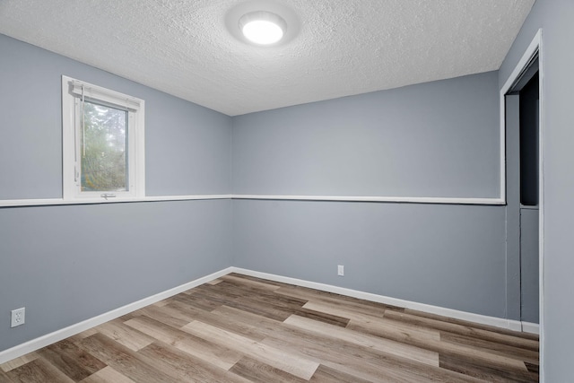 empty room with a textured ceiling, baseboards, and wood finished floors