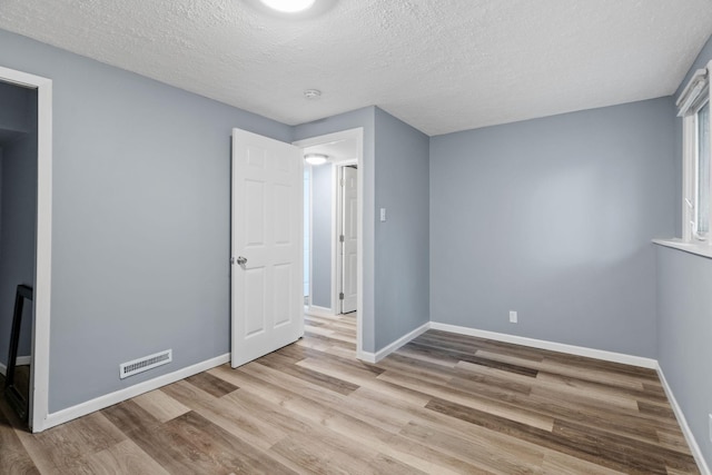 unfurnished bedroom with visible vents, baseboards, a textured ceiling, and wood finished floors