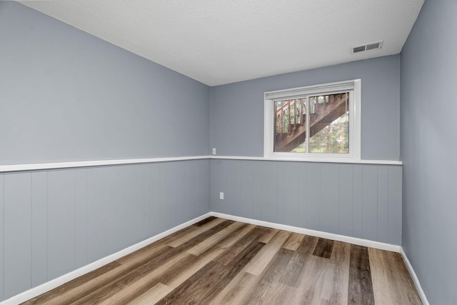 empty room featuring visible vents, a textured ceiling, baseboards, and wood finished floors