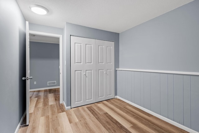 unfurnished bedroom featuring visible vents, baseboards, wood finished floors, a closet, and a textured ceiling