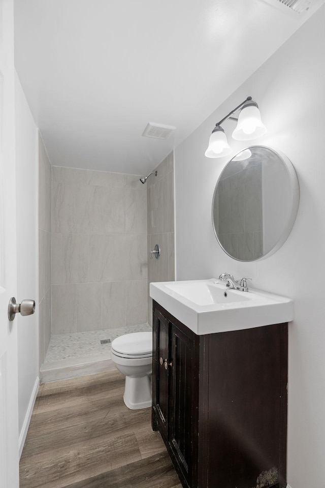 bathroom with toilet, wood finished floors, visible vents, and a tile shower