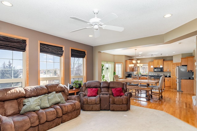 living room featuring recessed lighting, ceiling fan with notable chandelier, light wood finished floors, and a textured ceiling