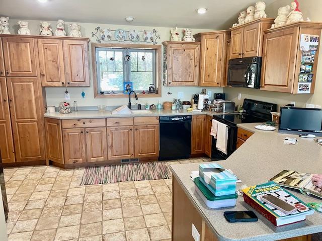 kitchen with brown cabinetry, black appliances, light countertops, and a sink