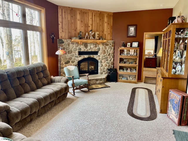 carpeted living area featuring a stone fireplace and wooden walls