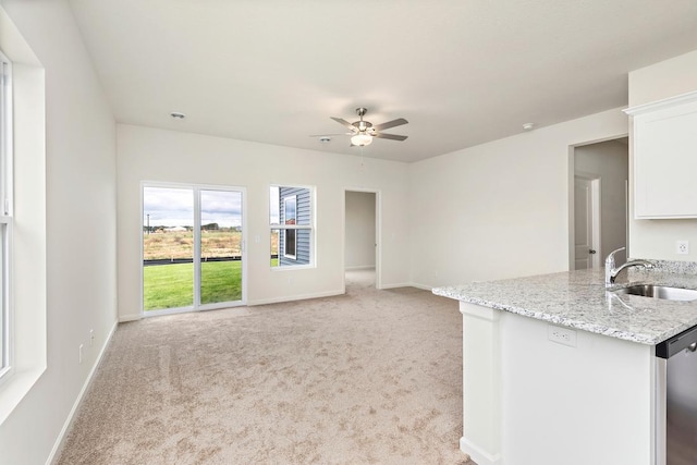 unfurnished living room featuring a sink, baseboards, light colored carpet, and a ceiling fan