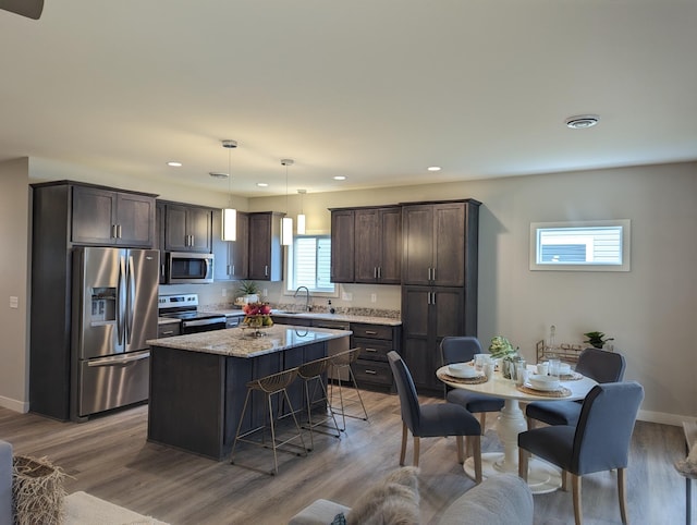 kitchen with a center island, dark brown cabinetry, light wood-type flooring, stainless steel appliances, and a sink