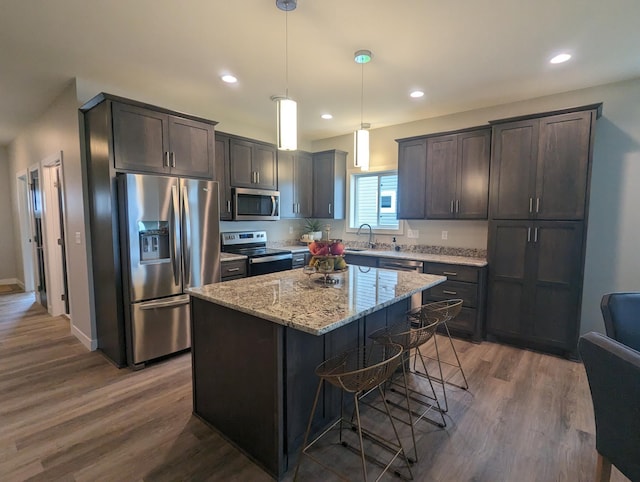 kitchen featuring light stone countertops, dark wood finished floors, a sink, stainless steel appliances, and a center island