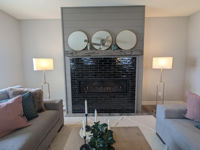 living area with a tile fireplace, baseboards, and wood finished floors