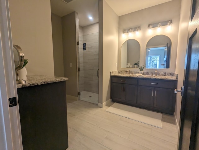 full bathroom with a shower stall, double vanity, baseboards, and a sink