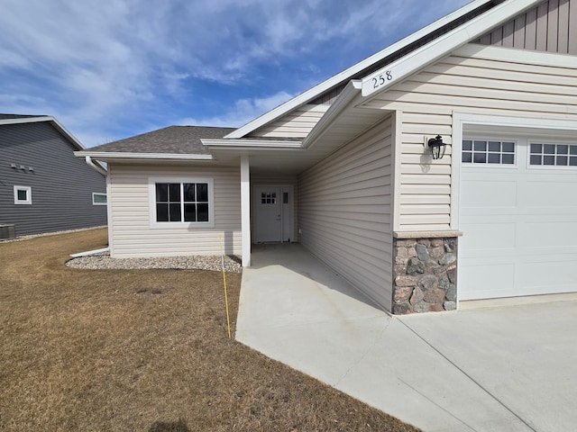 property entrance with central air condition unit, a garage, stone siding, and roof with shingles